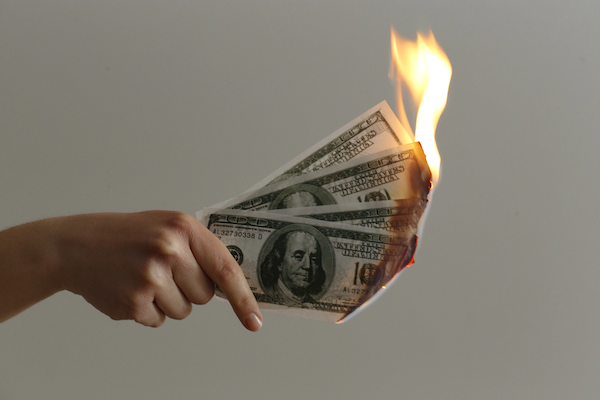person holding three 100 dollar bills that are on fire