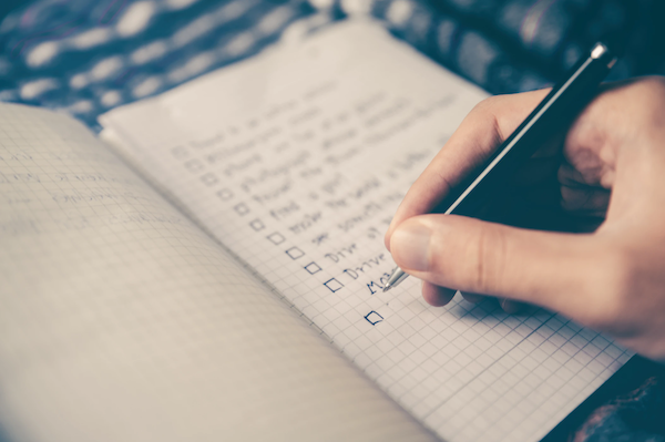 person writing checklist in a notebook