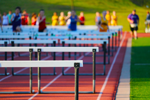 runners with hurdles on a track in front of them