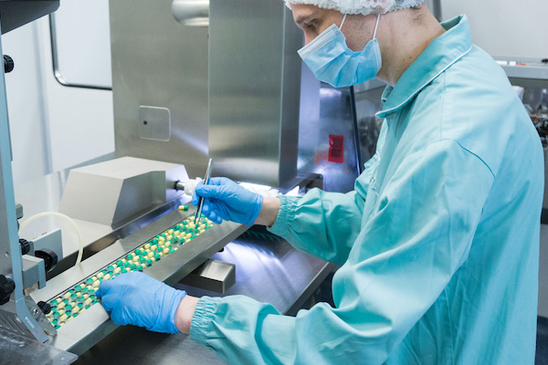 lab tech looking at pills on a conveyor belt