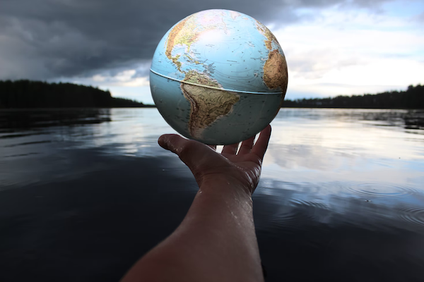 person holding a globe in their hand, over a lake